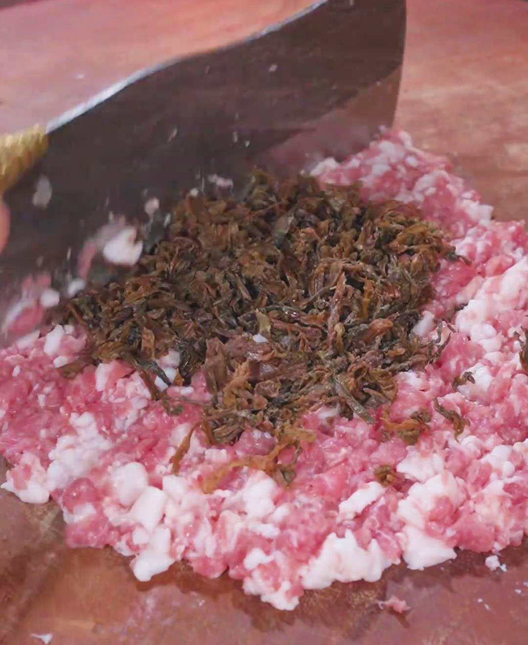 Add the soaked preserved vegetables and chop them together with the pork