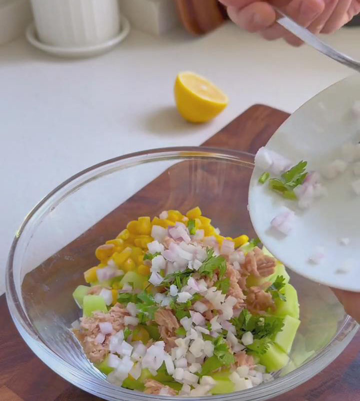 In the bowl containing the cucumber, corn, and tuna, add the chopped onion and cilantro